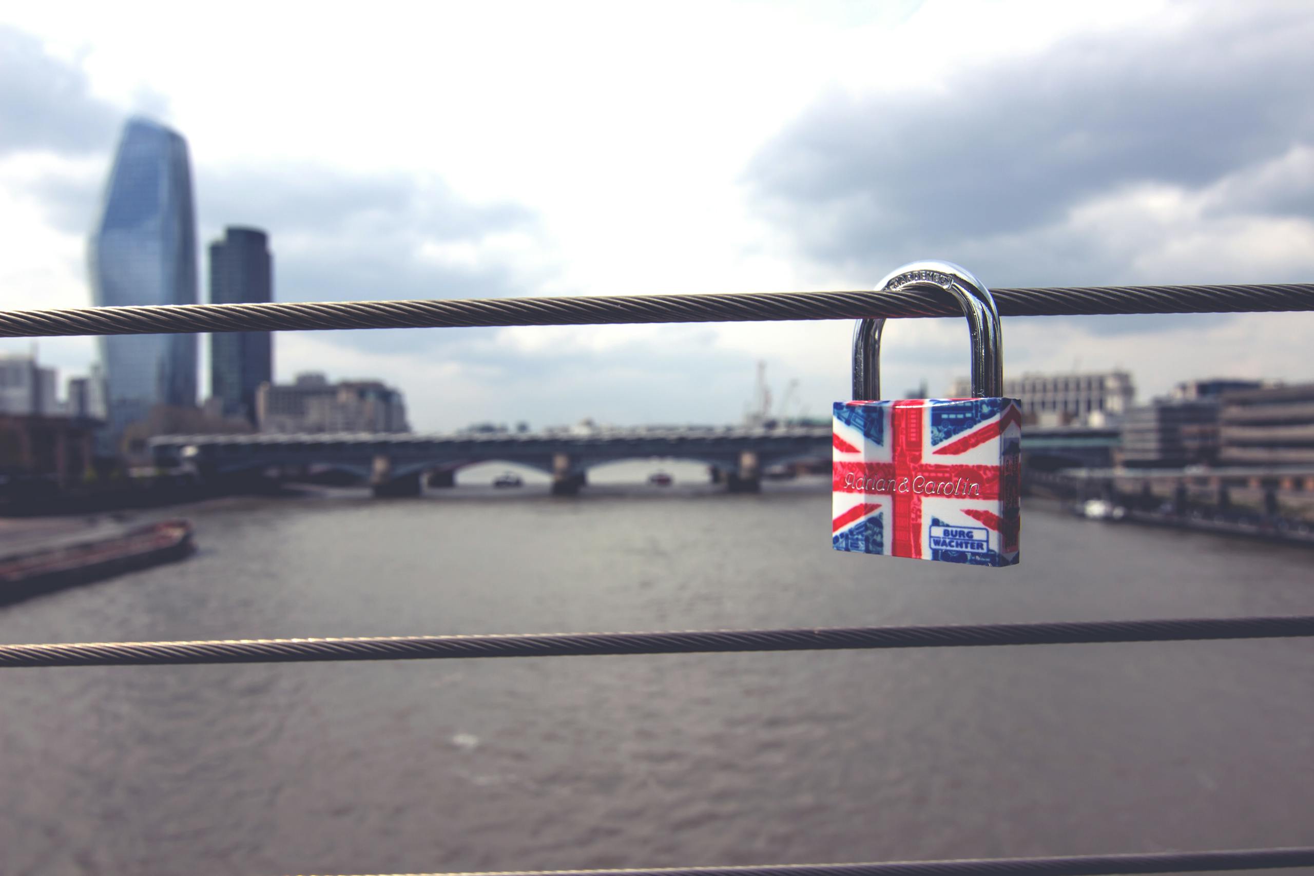 A colorful Union Jack padlock adorning bridge railings with London's skyline in the background.